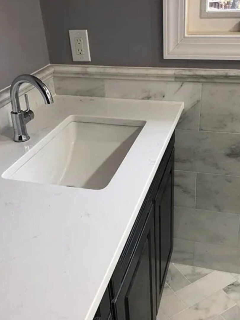 A bathroom with marble counter tops and black cabinets.