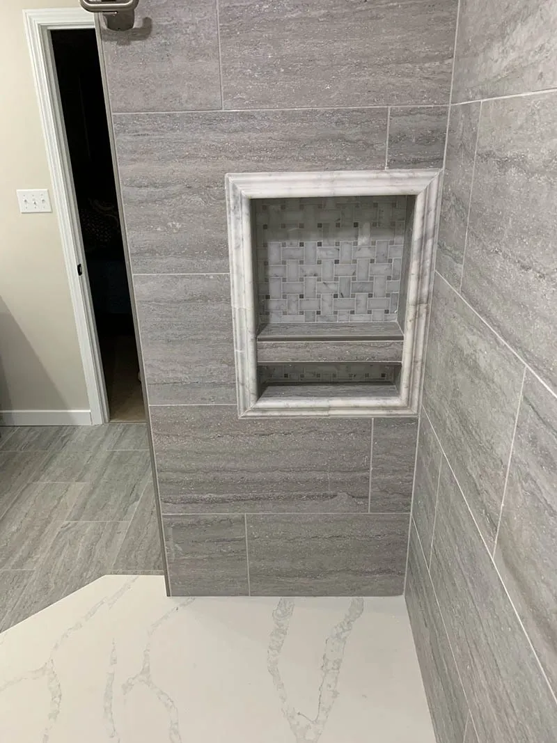 A bathroom with gray tile and a white shower.